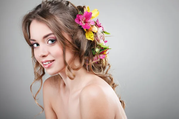 Hermosa chica, aislada sobre un fondo gris claro con flores varicolores en pelos, emociones, cosméticos — Foto de Stock