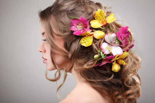 Hermosa chica, aislada sobre un fondo gris claro con flores varicolores en pelos, emociones, cosméticos —  Fotos de Stock