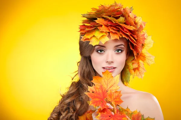 Close-up portret van mooie meisje in in een chaplet van gekleurde herfst bladeren op een gele achtergrond — Stockfoto