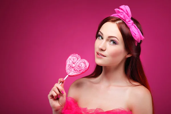 Portret van mooie vrolijke roodharige meisje met een grote suikergoed op een roze achtergrond — Stockfoto