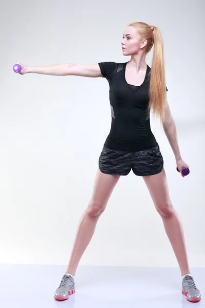 Hermosa joven se dedica a un gimnasio, sobre un fondo gris claro — Foto de Stock