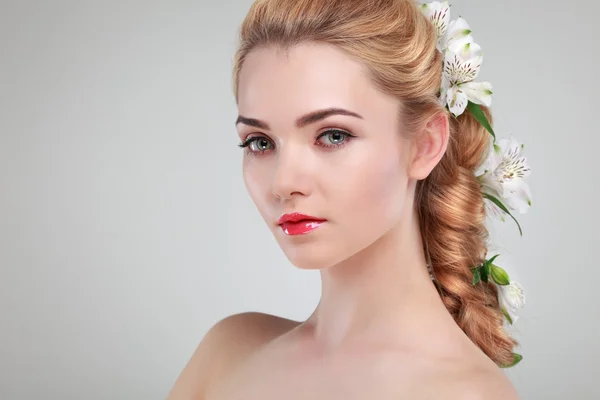 Hermosa chica, aislada sobre un fondo gris claro con flores varicolores en pelos, emociones, cosméticos Imágenes de stock libres de derechos