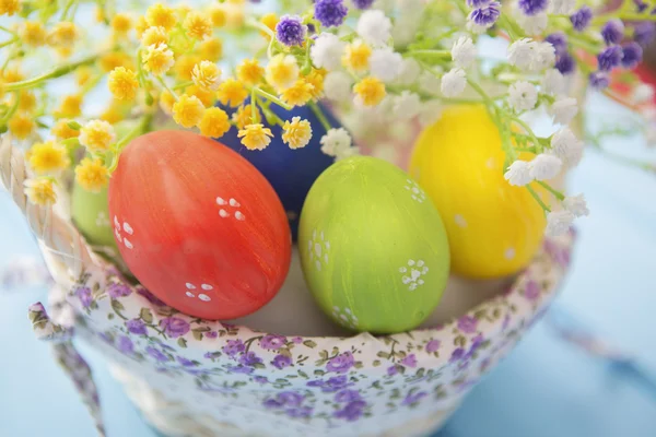 Colorful Easter eggs in basket on blue wood background. — Stock Photo, Image