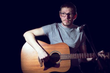 Adam şarkıcı gitar çalıyor ve şarkı söylüyor.