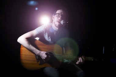 Adam şarkıcı gitar çalıyor ve şarkı söylüyor.