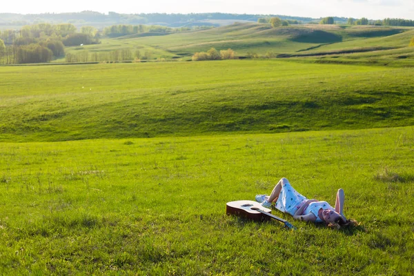 Beautiful hippie girl with guitar lying on grass — Stock Photo, Image