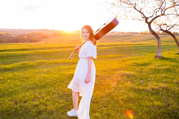 Mulher em vestido segurando a guitarra no céu nublado por do sol — Fotografia de Stock