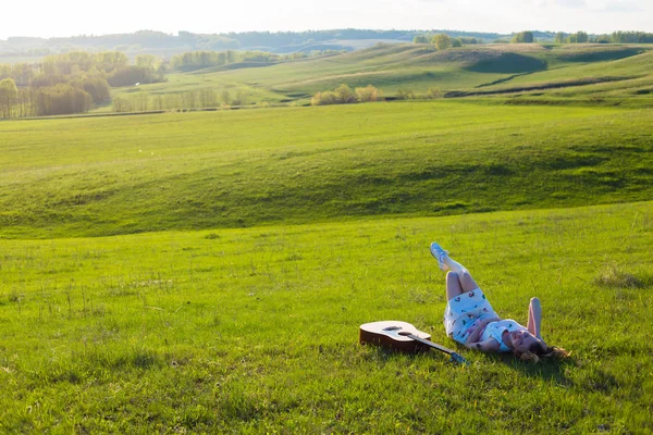 Beautiful hippie girl with guitar lying on grass — Stock Photo, Image