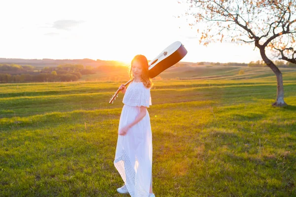 Mulher em vestido segurando a guitarra no céu nublado por do sol — Fotografia de Stock