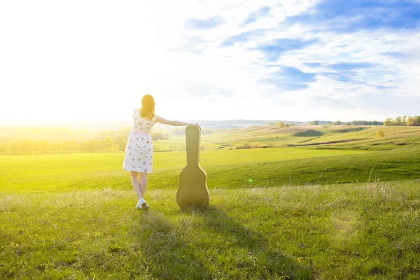 Mujer caminando en campo verde con guitarra acústica —  Fotos de Stock