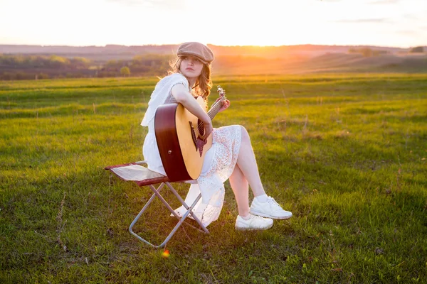 Menina sentada com guitarra acústica em campo — Fotografia de Stock