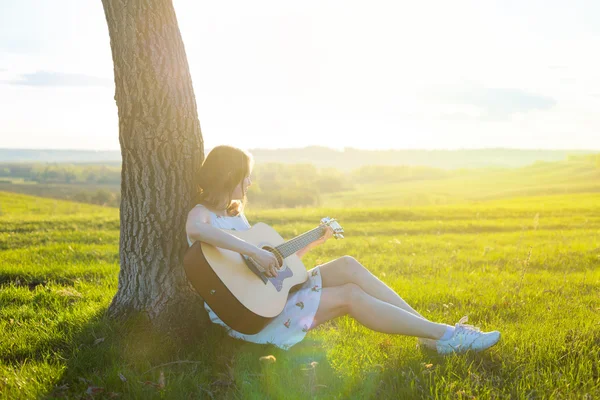 Beautiful young girl playing guitar in the field. — Stock Photo, Image