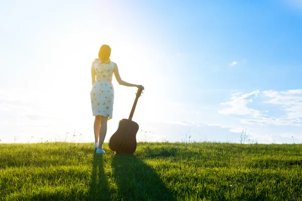 Mujer en vestido sosteniendo la guitarra en cielo nublado puesta del sol — Foto de Stock