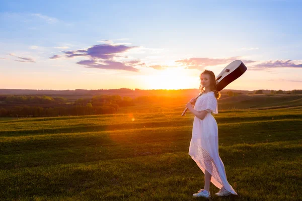 Woman in dress holding the guitar on cloudy sunset sky — Stock Photo, Image