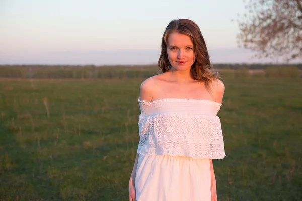 Mulher sorridente bonita em um campo no por do sol — Fotografia de Stock