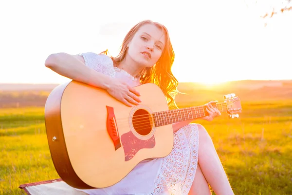 Schönes junges Mädchen spielt Gitarre auf dem Feld. — Stockfoto