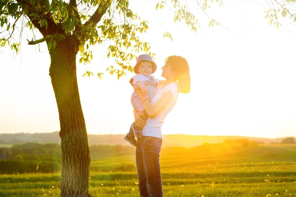 Retrato de mãe feliz com bebê no fundo por do sol — Fotografia de Stock