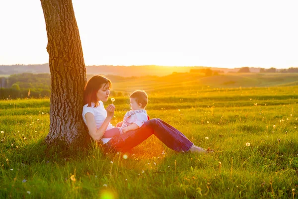 Jovem mãe com pequeno menino sentado ao pôr do sol — Fotografia de Stock