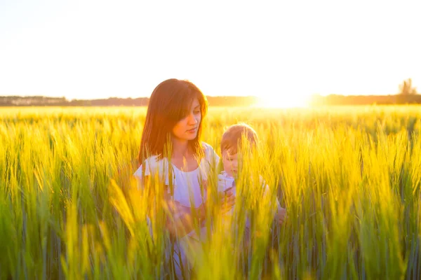 Glückliche Mutter hält Baby lächelnd auf Weizenfeld im Sonnenlicht. — Stockfoto