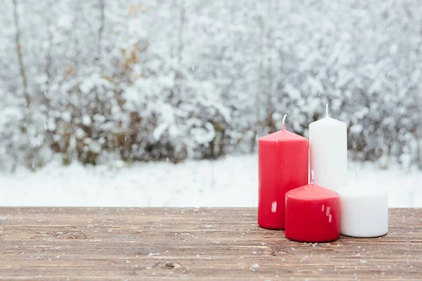 Schöne Rote Und Weiße Weihnachtskerzen Auf Dem Holztisch Vor Schneebedecktem Stockfoto