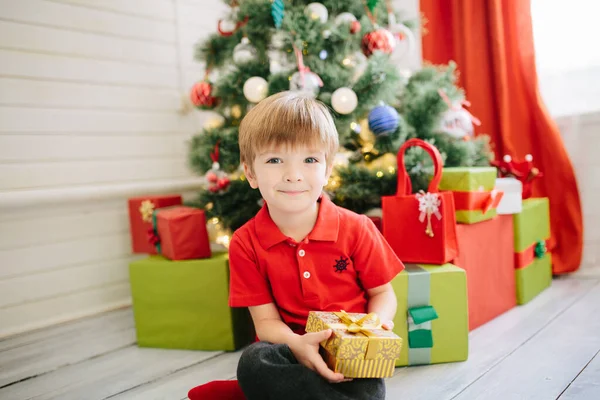 Lindo niño de unos cinco años con un regalo en una habitación de Navidad decorada con un árbol de Navidad —  Fotos de Stock