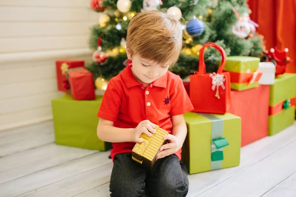 Lindo niño de unos cinco años con un regalo en una habitación de Navidad decorada con un árbol de Navidad — Foto de Stock