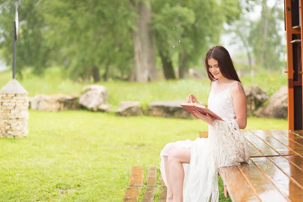 Una mujer guapa con vestido blanco leyó el libro. Chica se sienta en la terraza — Foto de Stock