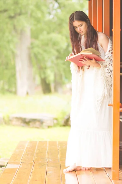 Una mujer guapa con vestido blanco leyó el libro. Chica se sienta en la terraza — Foto de Stock
