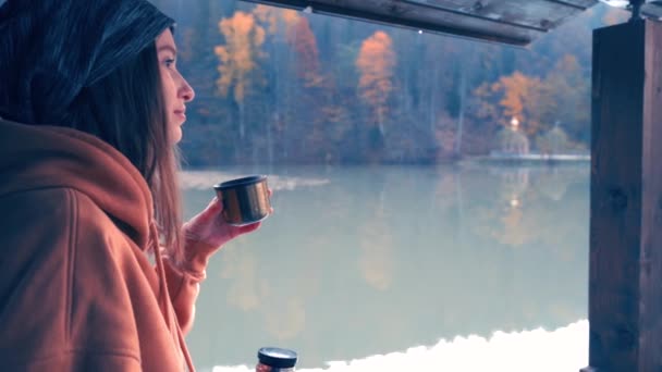 Девушка отдыхает в походе. Пьет чай или кофе из термоса на берегу горного озера. Видео замедленного действия — стоковое видео