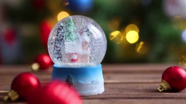 Noel ağacının arka planında Noel ışıkları olan kar küresi