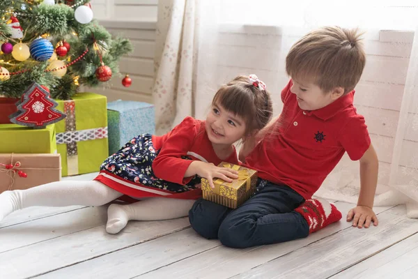 Niño da un regalo de Navidad a una chica en una habitación soleada brillante —  Fotos de Stock
