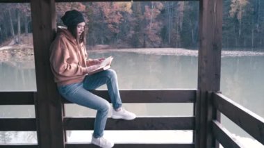 Kız bir yürüyüşte dinleniyor. Dağ gölünün kıyısında bir kitap oku. Yavaş çekim videosu