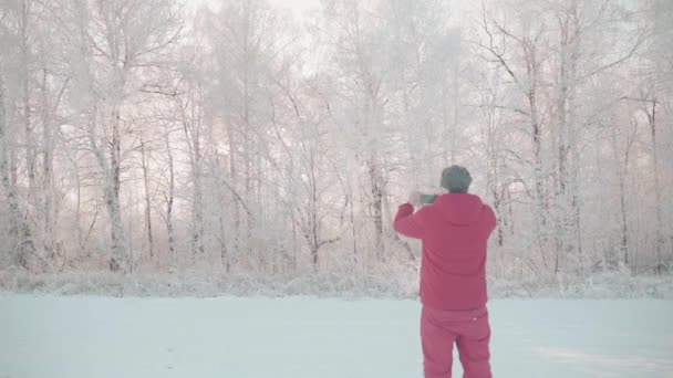 En man går genom en vinterskog med snötäckta träd på en vacker frostig morgon — Stockvideo