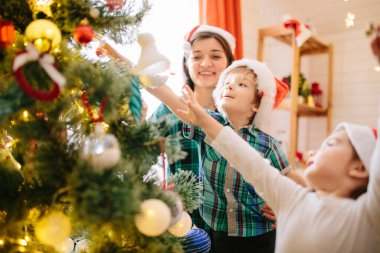 Mutlu aile annesi, oğlu ve kızı Noel kışında güneşli bir sabahta süslü bir Noel kutlaması odasında Noel ağacı ve hediyelerle