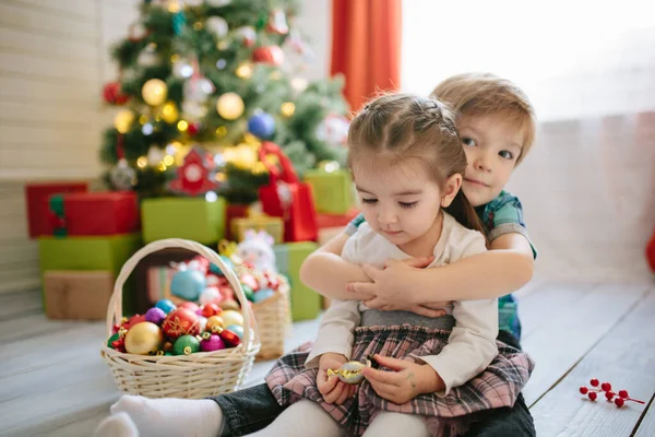 Niño y niña feliz en una mañana soleada de invierno de Navidad en una sala de celebración de Navidad decorada con un árbol de Navidad y regalos —  Fotos de Stock