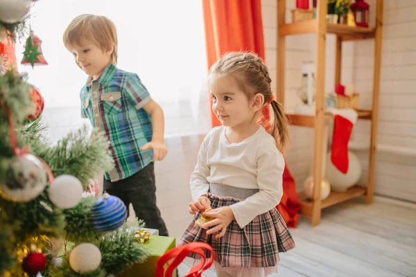 Niño y niña feliz en una mañana soleada de invierno de Navidad en una sala de celebración de Navidad decorada con un árbol de Navidad y regalos —  Fotos de Stock