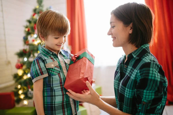 Feliz familia mamá e hijo en una mañana soleada de invierno de Navidad en una sala de celebración de Navidad decorada con un árbol de Navidad y regalos —  Fotos de Stock