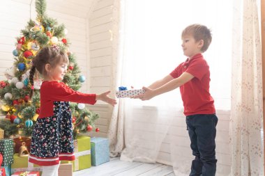 Oğlan, parlak güneşli bir odada bir kıza Noel hediyesi verir.