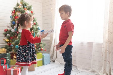 Oğlan, parlak güneşli bir odada bir kıza Noel hediyesi verir.
