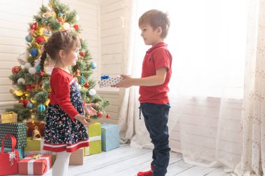 Oğlan, parlak güneşli bir odada bir kıza Noel hediyesi verir.