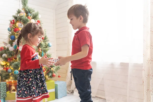 Niño da un regalo de Navidad a una chica en una habitación soleada brillante —  Fotos de Stock