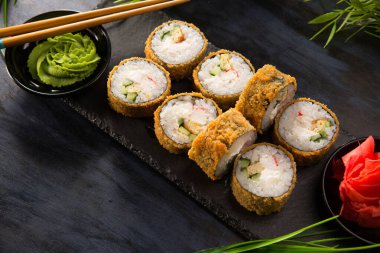 Siyah arka planda wasabi ve zencefilli fırında suşi ruloları. Japon Doğu mutfağı.