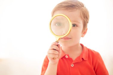 Yeni bilgi. Beyaz bir camda büyüteçten bakan bir çocuk