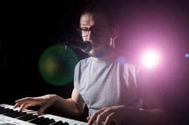 Klavyeci koyu arkaplanda çalıp şarkı söylüyor