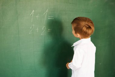 Küçük tatlı okul çocuğu okul yönetim kurulunun yanında duruyor ve matematik ödevlerini çözmek istiyor.