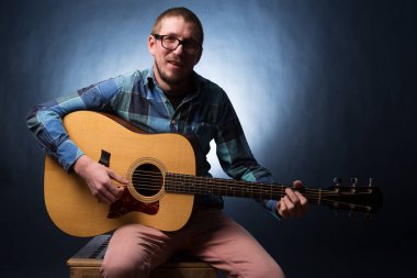 Koyu mavi arka planda gitar çalan yakışıklı genç bir müzisyen.