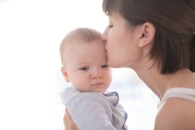 Sevgi dolu anne bebeğiyle oynuyor. Güneşin doğduğu bir pencerede oturuyor.