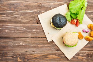 Lezzetli fast food. Sebzeli sığır burger. Tahta desenli arka planda susam tohumlarıyla düz yatıyordu..