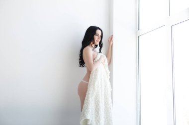 Uzun saçlı, dantelli iç çamaşırlı, pencerenin yanında poz veren güzel bir kadının portresi.