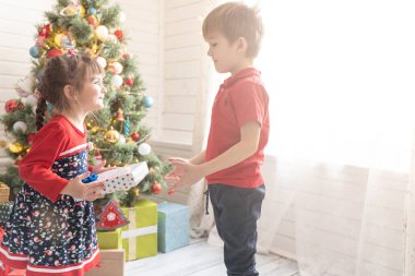 Oğlan, parlak güneşli bir odada bir kıza Noel hediyesi verir..